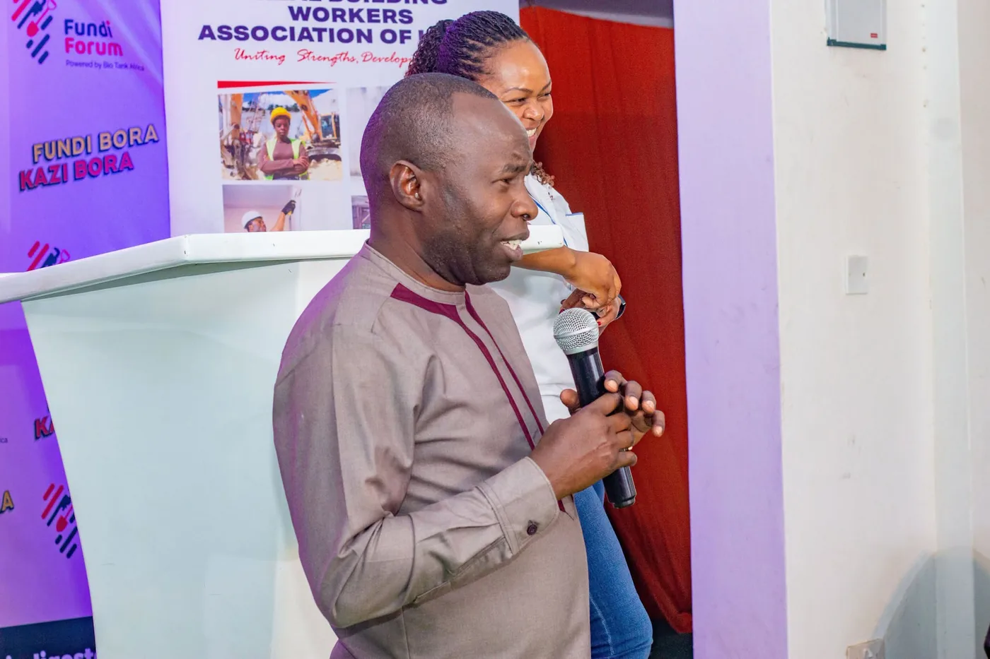 A speaker addressing attendees at the Fundi Forum beside the REBWAK banner