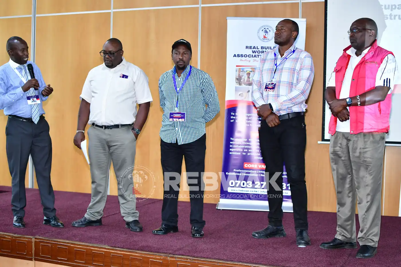 Speakers standing on stage beside the REBWAK banner at the KRA training